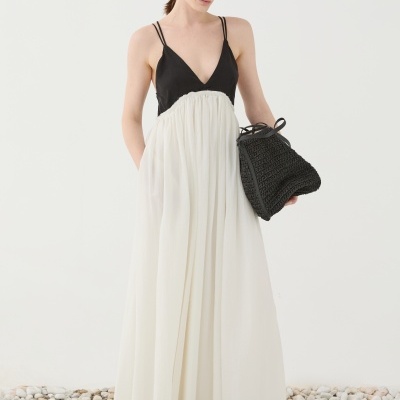 Mulher a usar vestido longo preto e branco e a segurar mala preta com textura trançada, em fundo branco com pedras no chão.