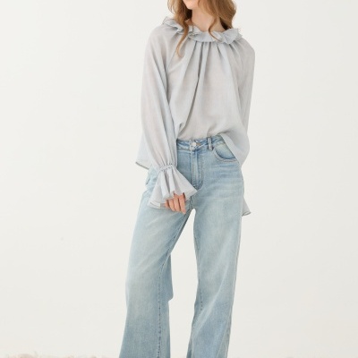 Modelo vestindo blusa cinza clara transparente e calças de ganga largas azul claro em fundo branco com pedras