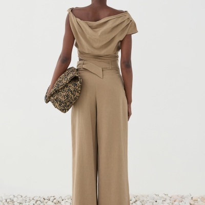 Mulher com conjunto bege e mala trançada a pé sobre pedras brancas