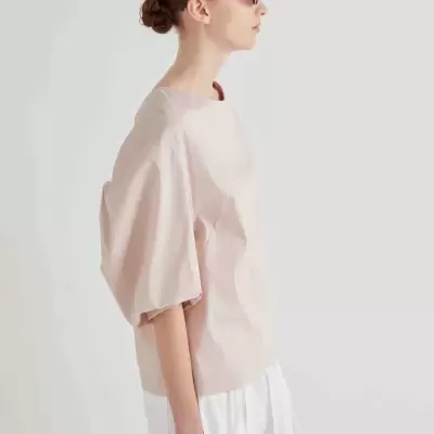 Mulher com blusa rosa clara e saia ou calças brancas, vista de perfil