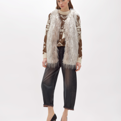Mulher com colete peludo branco, camisola castanha com padrão, calças pretas e sapatos de salto