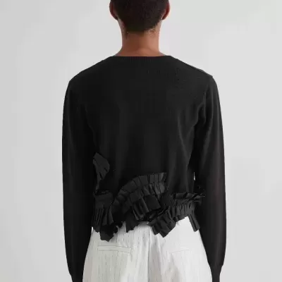 Camisola preta com detalhes ondulados na parte traseira e calças brancas às riscas vistas de costas.