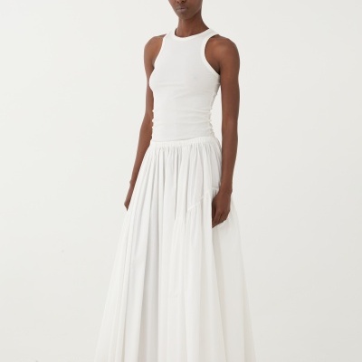 Mulher com blusa e saia brancas em ambiente minimalista com chão de pedras brancas