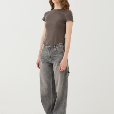 Mulher com t-shirt cinza, jeans largos cinza e ténis brancos sobre pedras brancas