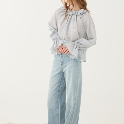 Mulher com blusa cinzenta clara de tecido leve e calças de ganga largas azul claro em chão de pedras.