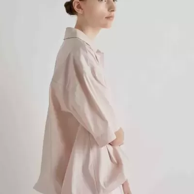 Mulher de perfil com camisa oversized de manga curta bege claro num fundo branco