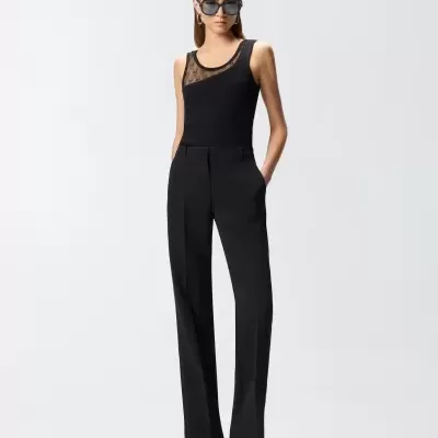 Mulher com top preto sem mangas com tule e monograma, calças pretas de corte reto e sandálias de salto preto