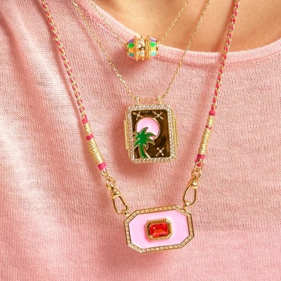 Três colares dourados com pingentes coloridos usados sobre camisola rosa claro.
