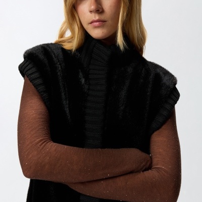 Pessoa com camisola castanha e colete preto em fundo branco