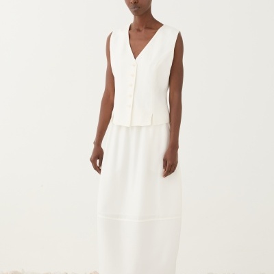 Mulher com vestido branco comprido e sapatilhas, em chão de pedras brancas e rosa claro