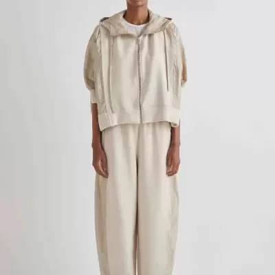 Conjunto bege composto por casaco com capuz e calças largas, usado com sapatilhas pretas.