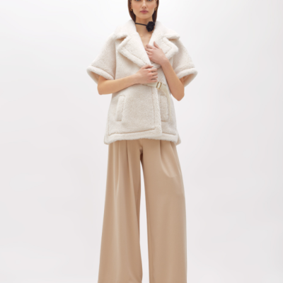 Mulher com casaco curto de pelo branco e calças largas bege em fundo branco