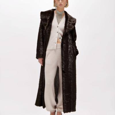 Mulher com casaco de pêlo castanho escuro, conjunto bege e sapatos prateados em fundo branco