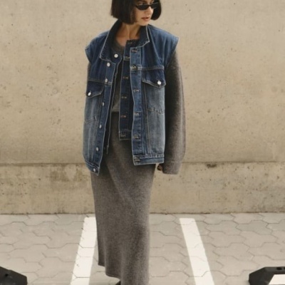 Mulher com vestido cinzento de malha e casaco de ganga azul sem mangas num pavimento hexagonal