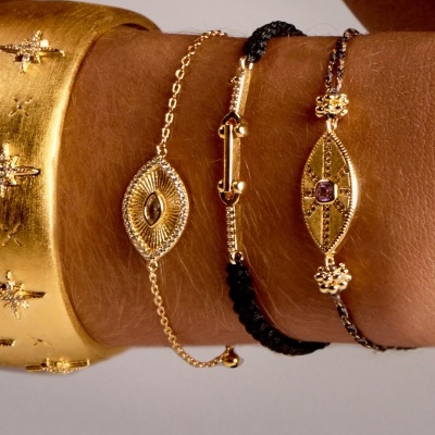 Pulseiras douradas e cordão preto trançado num pulso castanho