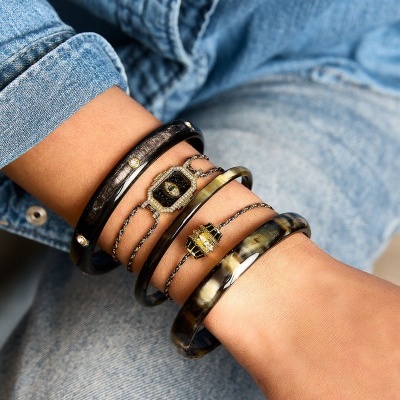 Pulseiras em tons escuros com detalhes dourados no pulso de pessoa com roupa de ganga azul