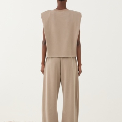 Conjunto feminino bege de top sem mangas com ombreiras e calças largas em cenário minimalista de pedras brancas.