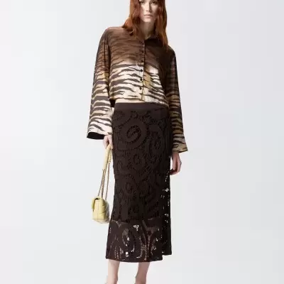 Conjunto feminino com camisa animal print, saia de crochê preta, sapatos pretos e bolsa bege pequena.