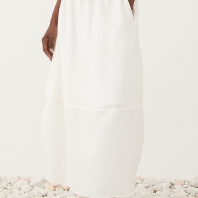 Saia branca comprida e sapatilhas brancas em chão de pedras claras