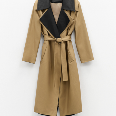 Casaco comprido bege com colarinho preto pendurado numa parede branca