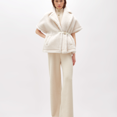 Modelo veste colete de pele sintética branca com cinto e calças largas bege claro