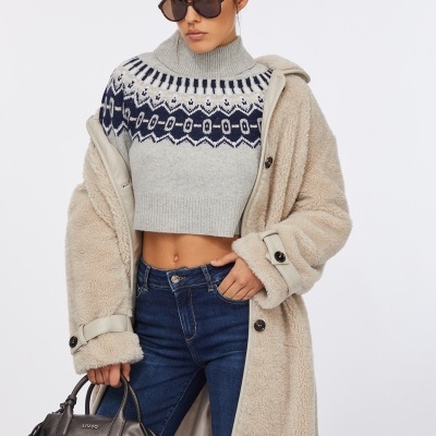 Mulher com casaco bege peludo, camisola cinza com padrão azul, jeans escuro, óculos de sol e mala castanha LIU JO