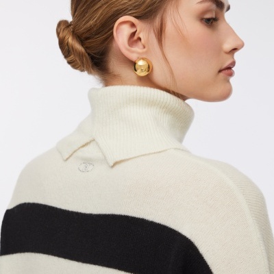 Camisa de malha branca com risca preta e brincos dourados em mulher vista de lado