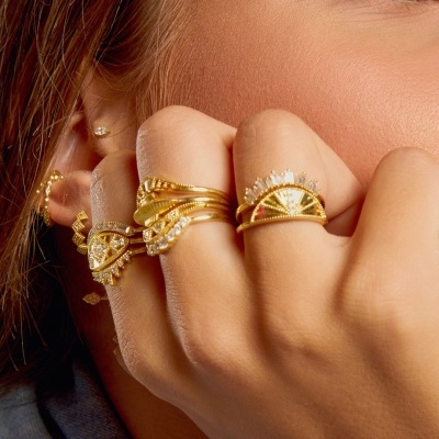 Mão com anéis dourados e pedras brilhantes junto ao rosto