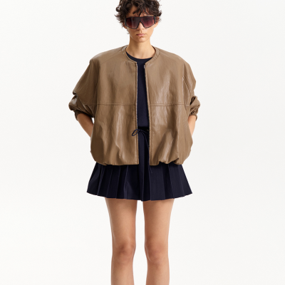 Mulher com casaco bege e vestido preto plissado, usando óculos escuros grandes