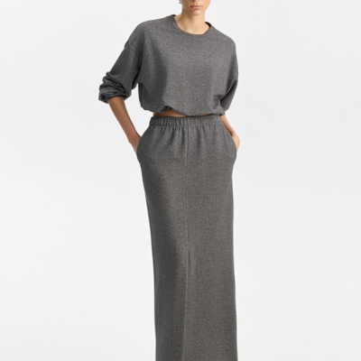 Conjunto feminino cinza com blusão e saia longa, sapatos pretos e óculos de sol.