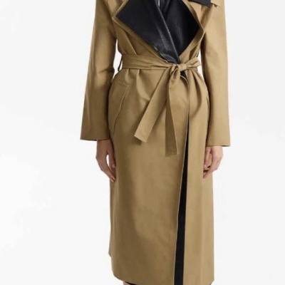 Mulher com casaco bege e preto, óculos escuros e botas pretas em fundo branco