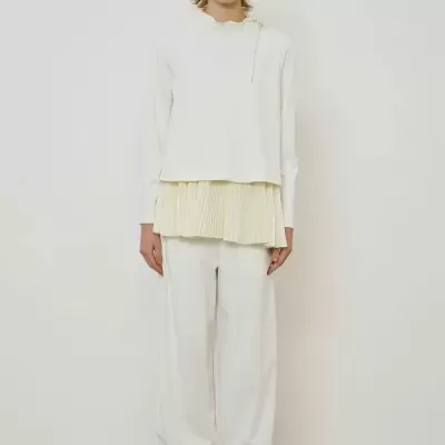 Mulher com roupa branca e sapatilhas peludas castanhas em fundo branco simples.