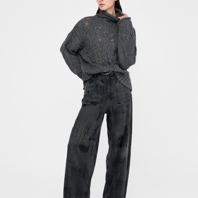 Mulher com camisola cinza de malha e calças largas cinza escuro em fundo branco