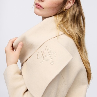 Casaco creme de lã com gola larga e bordado usado por mulher loira