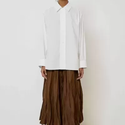 Pessoa com camisa branca, saia castanha plissada e calçado castanho peludo