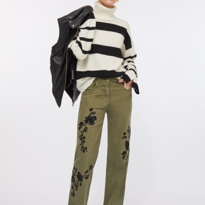 Mulher com camisola às riscas branca e preta, calças verdes bordadas, botas pretas e jaqueta de couro preta