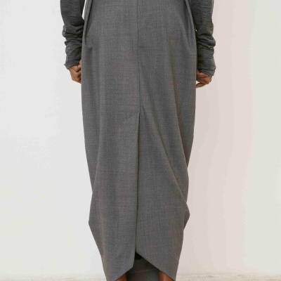 Saia comprida cinzenta com fecho e bolsos laterais, vista de costas, combinada com camisa cinzenta escura e sapatos pretos.