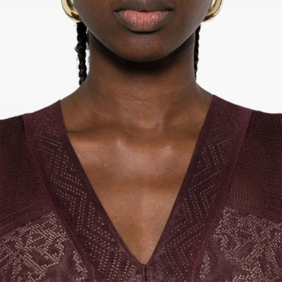 Mulher com blusa de malha vinho com padrão geométrico e brincos dourados de argola grande