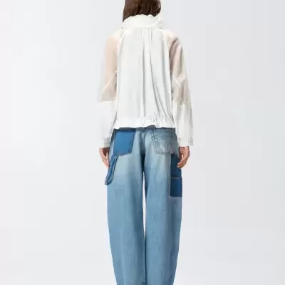 Pessoa de costas com blusa branca e calças largas de ganga azul