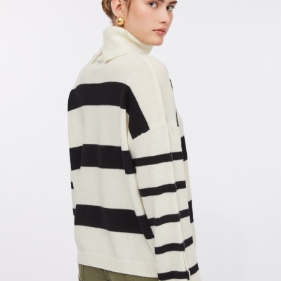 Mulher com camisola de malha creme com riscas pretas largas e gola alta e calças verde militar.