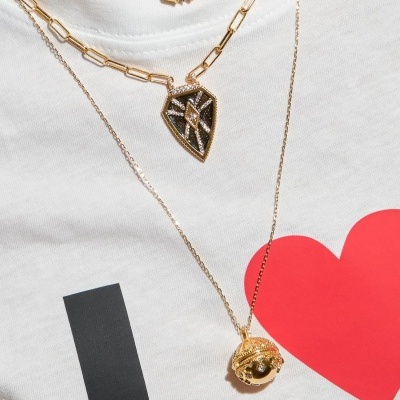 Três colares dourados com pendentes diferentes sobre t-shirt branca com estampa