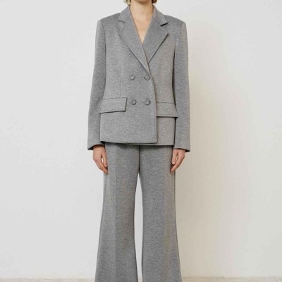 Mulher vestindo conjunto cinzento blazer e calças largas, em fundo branco