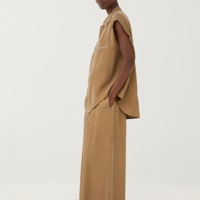 Conjunto feminino castanho claro de camisa sem mangas e saia comprida sobre pedras brancas