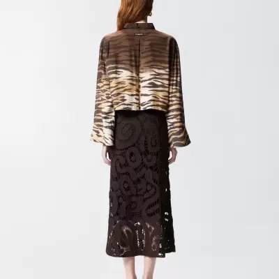 Mulher vista de costas vestindo camisa animal print, saia preta de renda e sapatos pretos de salto.