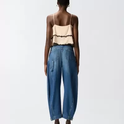 Mulher de costas com top bege, jeans azuis largos e sapatos pretos de salto alto