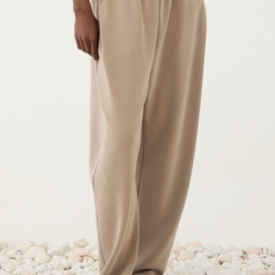 Calças largas bege com cintura elástica e bolsos em piso de pedras brancas arredondadas