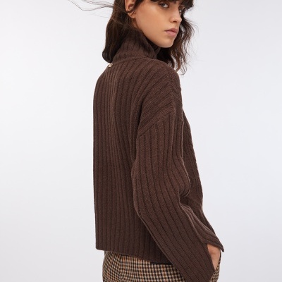 Modelo de costas a usar suéter castanho canelado de gola alta e calças aos quadrados