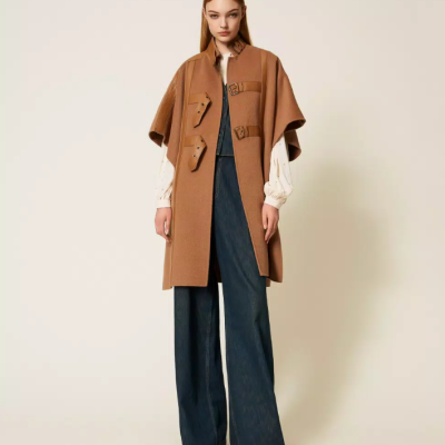 Mulher com capa castanha, blusa branca e calças de ganga largas
