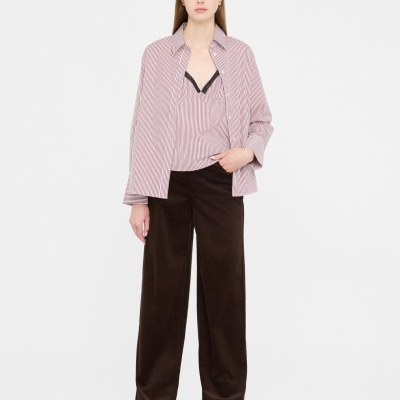 Conjunto de roupa com camisa de riscas rosa e branca, top rosa, calças largas castanhas escuras e sapatos pretos em fundo branco.