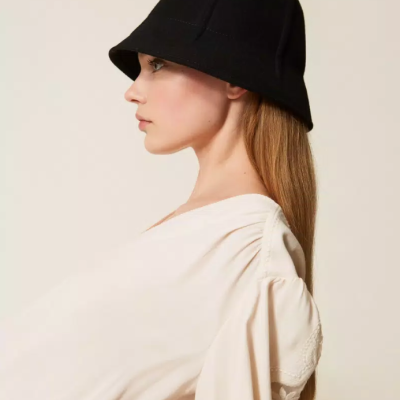 Mulher de perfil usando chapéu preto tipo balde e blusa clara com mangas bufantes